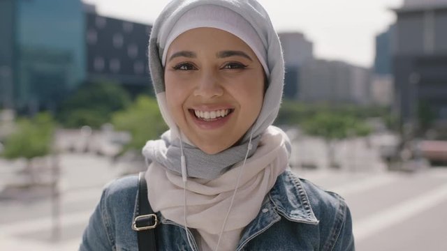 portrait of beautiful young muslim woman student smiling confident at camera listening to music using earphones wearing hijab headscarf 