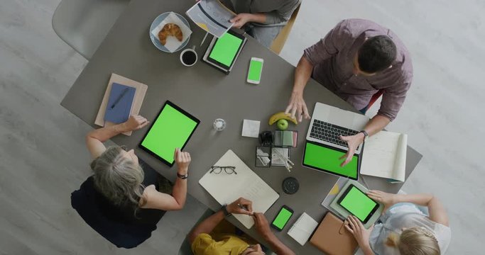 creative diverse business people brainstorming innovative ideas for startup company viewing green screen using mobile computer technology in boardroom meeting above view