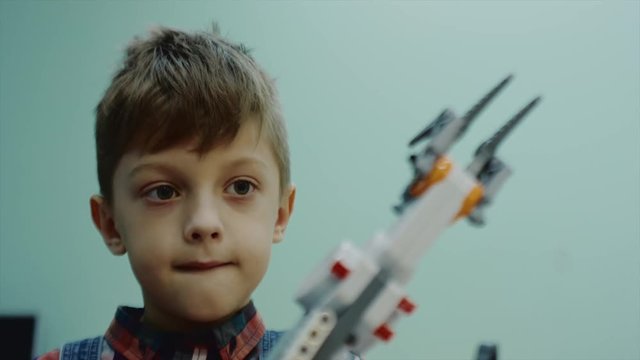 Little boy is tensionally looking on robotic arm and controlling it. Detail view of his face and robots parts, close-up