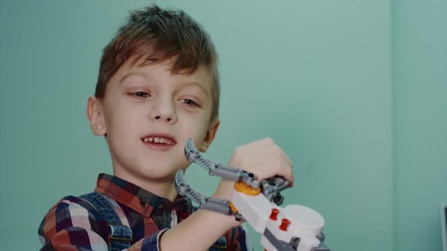 Close up shot of a little smart boy playing with blocks robotic claw in robotics club. Happy boy fighting with robotic claw. Fun time.