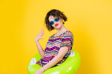 a young girl with curly hair in a green rubber ring and  blue watersport goggles on a yellow isolated background looks at the camera