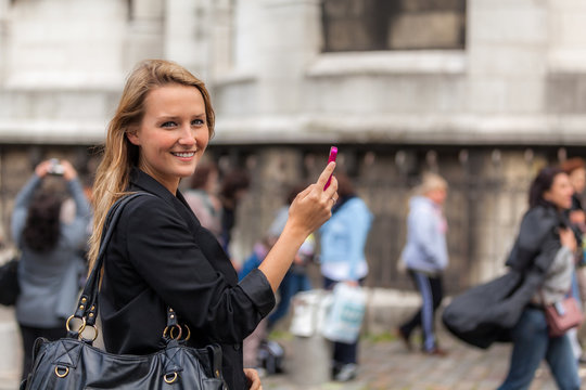 Smiling Young Woman with Mobile Phone with Out-of-Focus People Behind Her