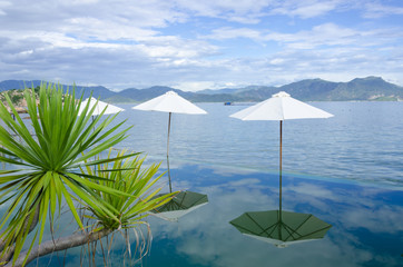 Beach umbrellas on the rim of an infinity pool at a tropical resort overlooking the calm ocean on summer day in a tourism and vacation concept