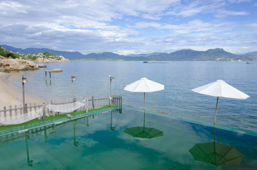 Beach umbrellas on the rim of an infinity pool at a tropical resort overlooking the calm ocean on...