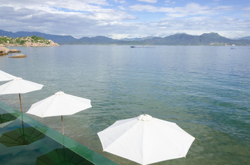 Beach umbrellas on the rim of an infinity pool at a tropical resort overlooking the calm ocean on...