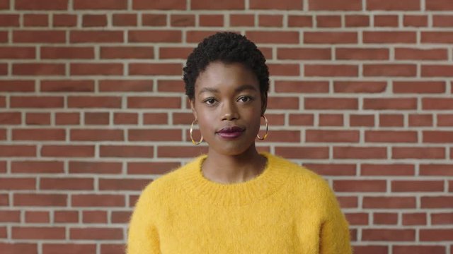 portrait of stylish african american woman wearing yellow jersey looking confident on brick wall background