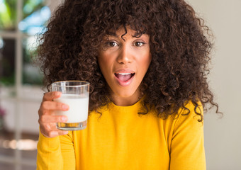 African american woman holding a glass of milk scared in shock with a surprise face, afraid and excited with fear expression