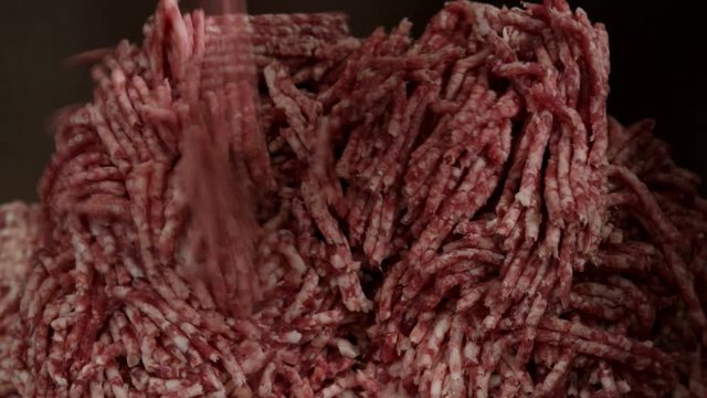 Minced meat is going out of a meat grinder and falling into a plastic container.