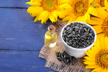 sunflower seed oil and sunflower seeds with beautiful yellow sunflowers in the background on a blue wooden background
