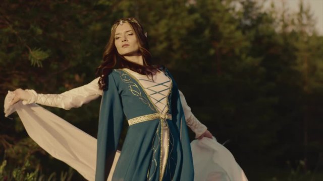 Elf woman is throwing white cloth on her back and walking proudly near forest. She is looking at camera, side view