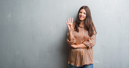 Young brunette woman over grunge grey wall showing and pointing up with fingers number four while smiling confident and happy.