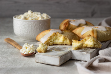 Pasties or buns with cottage cheese and powdered sugar glaze on a light background. Traditional Russian bun Sochnik. Selective focus. 