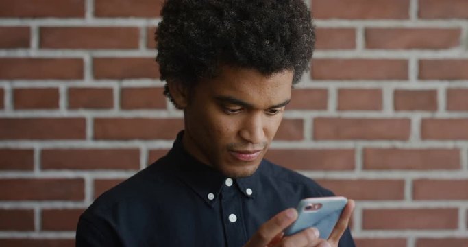 portrait young mixed race man using smartphone browsing online messages reading texting on mobile phone looking focused concentrating slow motion