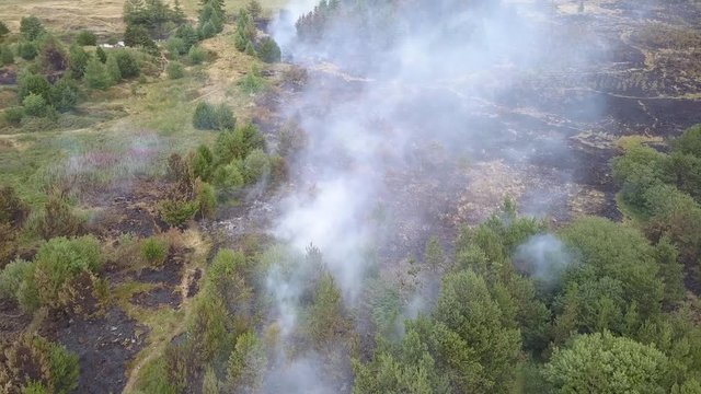 Aerial drone view of smoke from a wildfire burning on a grass and tree covered hillside