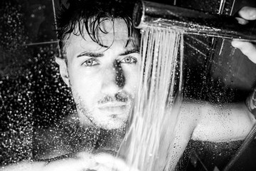 Hunky, handsome man, male with beard and muscular arms is wet in shower looking at camera