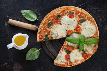 Traditional italian pizza with different types of cheese and tomatoes, above view on a dark brown stone background, horizontal shot