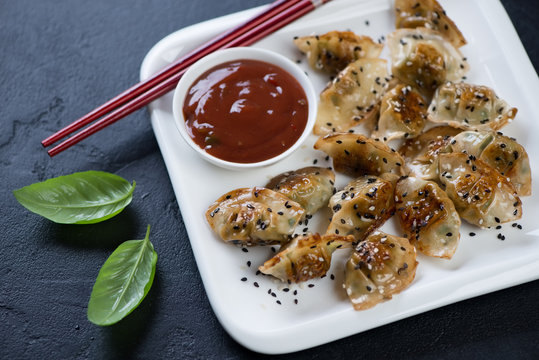 Fried wontons with sesame and dipping sauce served on a white plate, studio shot