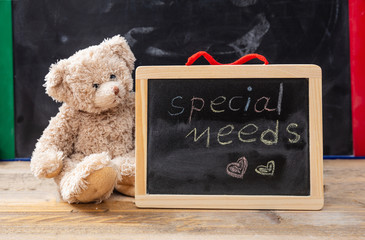 Teddy bear hiding behind a blackboard. Special needs text drawing on the blackboard