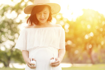 Smiling pregnant young woman holding headphones at her belly