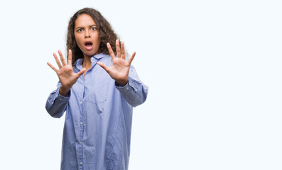 Young hispanic business woman afraid and terrified with fear expression stop gesture with hands, shouting in shock. Panic concept.