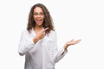 Beautiful young hispanic woman amazed and smiling to the camera while presenting with hand and pointing with finger.