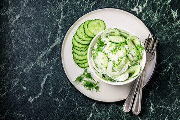 Creamy cucumber dill salad with yogurt dressing on dark marble background. Top view, space for text.