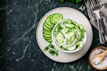 Creamy cucumber dill salad with yogurt dressing on dark marble background. Top view, space for text.