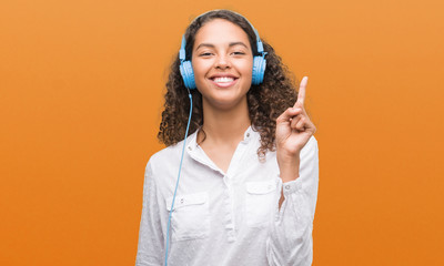 Young hispanic woman wearing headphones surprised with an idea or question pointing finger with...