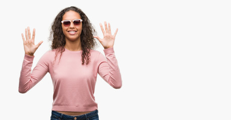 Fototapeta na wymiar Beautiful young hispanic woman wearing sunglasses showing and pointing up with fingers number ten while smiling confident and happy.