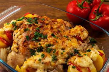 A hearty meat dish made of oven-baked chicken, tomatoes, potatoes and onions, under a ruddy crust of hard grated cheese in a glass pan for baking.