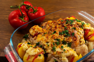 Meat dish of chicken with cheese crust, baked with vegetables in the oven, next to three red ripe tomatoes.