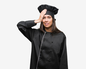 Young hispanic cook woman wearing chef uniform stressed with hand on head, shocked with shame and surprise face, angry and frustrated. Fear and upset for mistake.