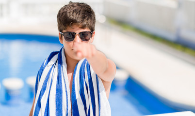 Young child on holidays at the swimming pool by the beach pointing with finger to the camera and to you, hand sign, positive and confident gesture from the front