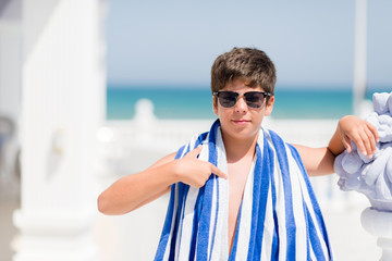 Young child on holidays wearing a navy towel by the beach with surprise face pointing finger to himself