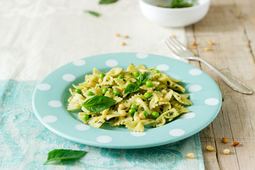 Pasta with pesto sauce, green peas and basil on a wooden table. Rustic style.