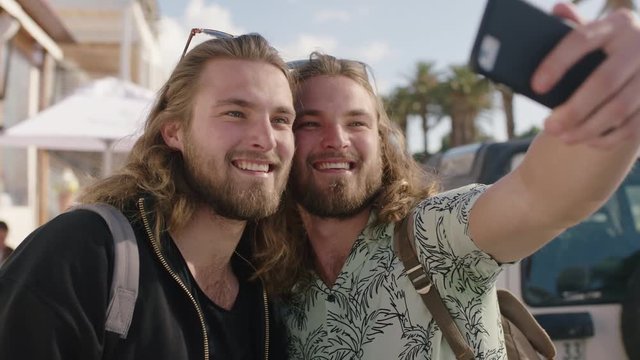 portrait of attractive twin brothers on vacation posing for selfie together taking photo using phone