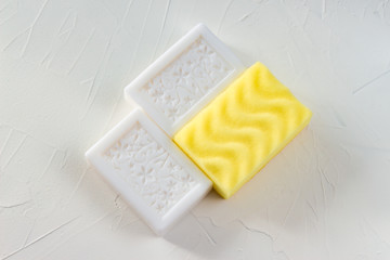 Yellow washcloth, sponge and two pieces of white soap on white background