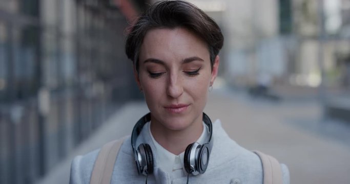 portrait attractive young business woman intern puts on earphones listening to music in city enjoying relaxed urban lifestyle slow motion