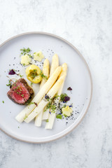 Modern German barbecue dry aged sliced fillet steak with white asparagus and roast potatoes in butter sauce as top view on a plate with copy space right
