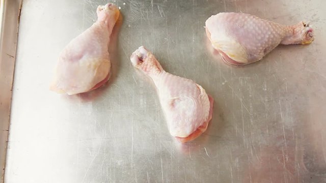 A woman places chicken legs, Roma tomato halves and red onion on a sheet pan