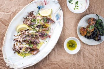Traditionelle gegrillte griechische Calamari mit Gemüse und Zitrone als Draufsicht auf Teller  