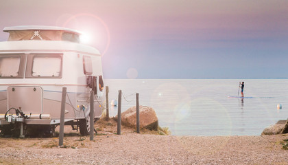small, cute caravan by the sea, beach in backlight with sunflares. Atmospheric stand up paddeling,...