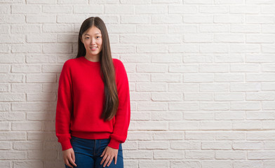 Young Chinese woman over brick wall with a happy and cool smile on face. Lucky person.