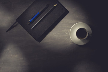 Cup of coffee on a dark office desk with agenda, pencil and pen