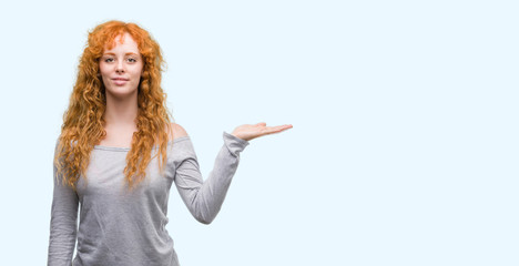 Young redhead woman smiling cheerful presenting and pointing with palm of hand looking at the...