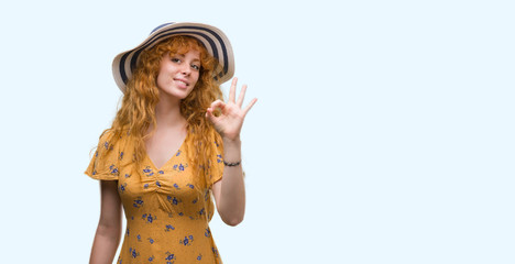 Young redhead woman wearing summer hat and dress doing ok sign with fingers, excellent symbol