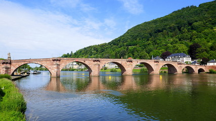 Fototapeta na wymiar alte Heidelberger Brücke mit angrenzendem Odenwald spiegelt sich im Neckar bei Sonne