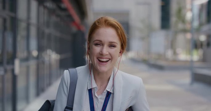 portrait happy young red head business woman laughing wearing earphones enjoying relaxed urban lifestyle listening to music in city slow motion