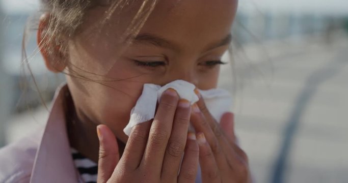 close up little girl blowing her nose using tissue young mixed race child flu outdoors