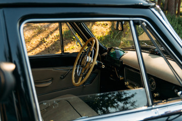 machine black, inside the seat of beige leather, retro car.stage in summer.driver's seat, white steering wheel.view from an open passenger window
